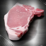 Rohes Kotelett vom regionalen Duroc-Schwein mit Knochen und feiner Marmorierung auf neutralem Untergrund.