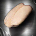 Roh geschnittene Gänsebrust aus Pommern in Extra-Qualität, feine Fleischstruktur, edel ausgeleuchtet vor metallischem Hintergrund